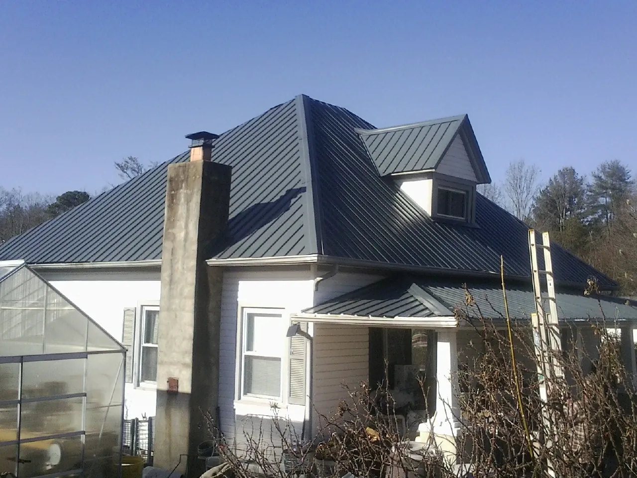 Dark blue standing seam metal roof on a white farmhouse with dormer — Slate & Tile Roof Repair by Roofing Brothers in Baxley