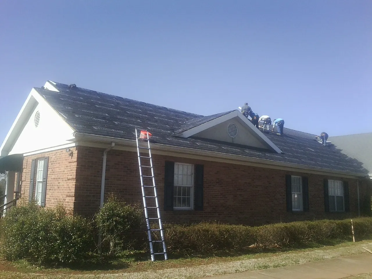 Crew tearing shingles off a brick ranch roof with a ladder set — Metal Roof Repair work by our crew in Baxley