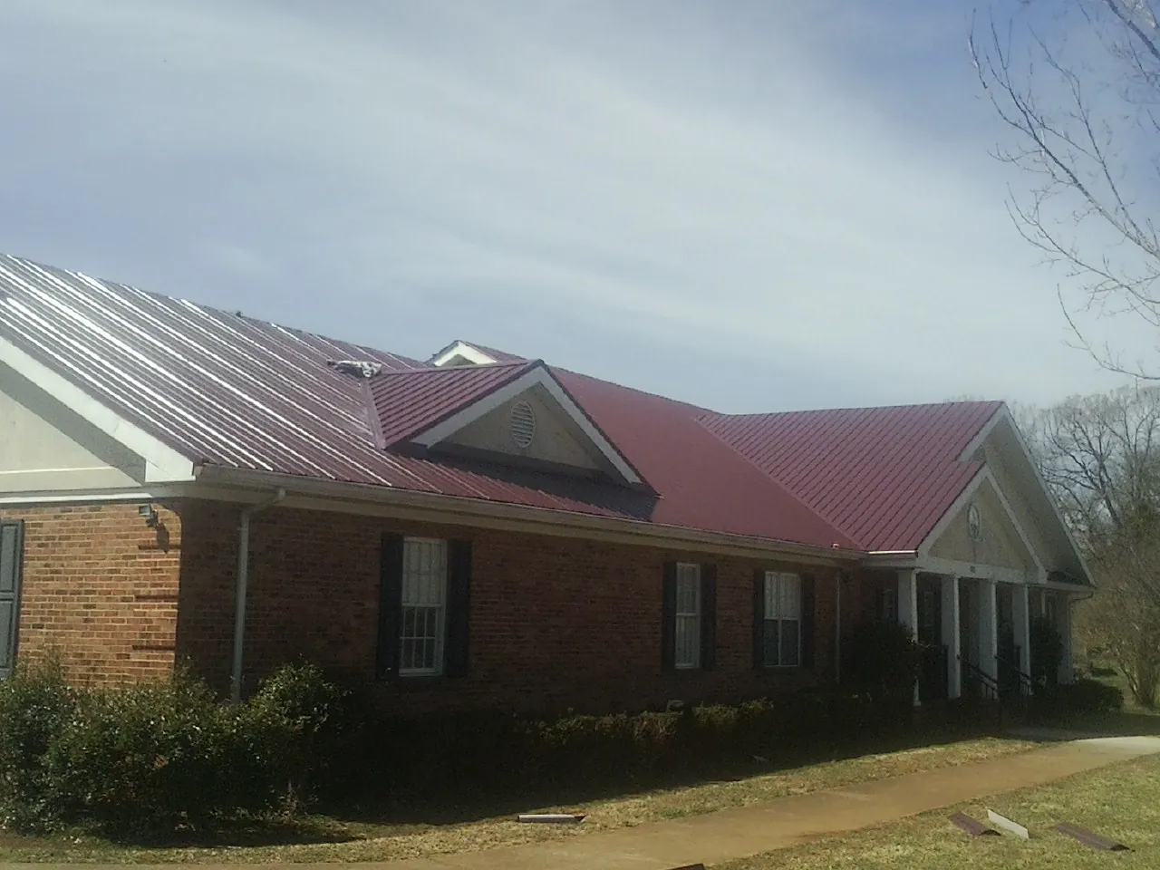 Red metal roof with gabled entries on a long brick building, from a Hail Damage Roof Repair job in Baxley