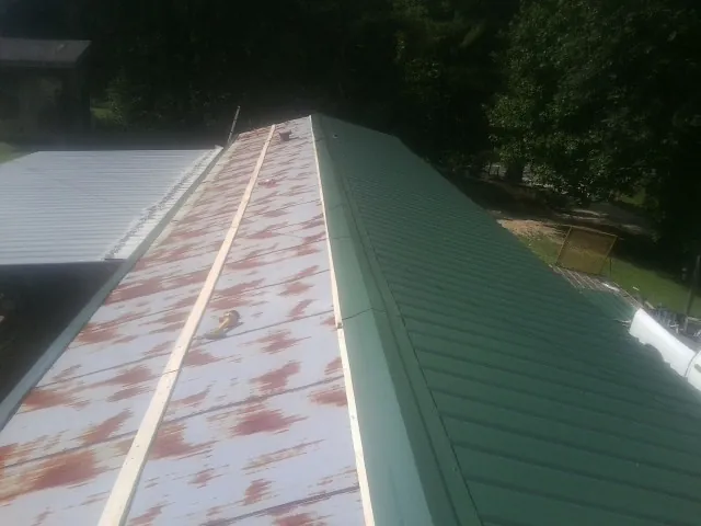 Old rusted panels beside newly installed green metal roofing — Wind Damage Roof Repair by Roofing Brothers in Baxley