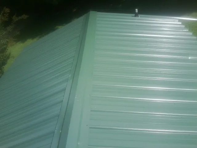 New green metal panels meeting at the ridge of a roof — Flat Roof Repair work by our crew in Baxley