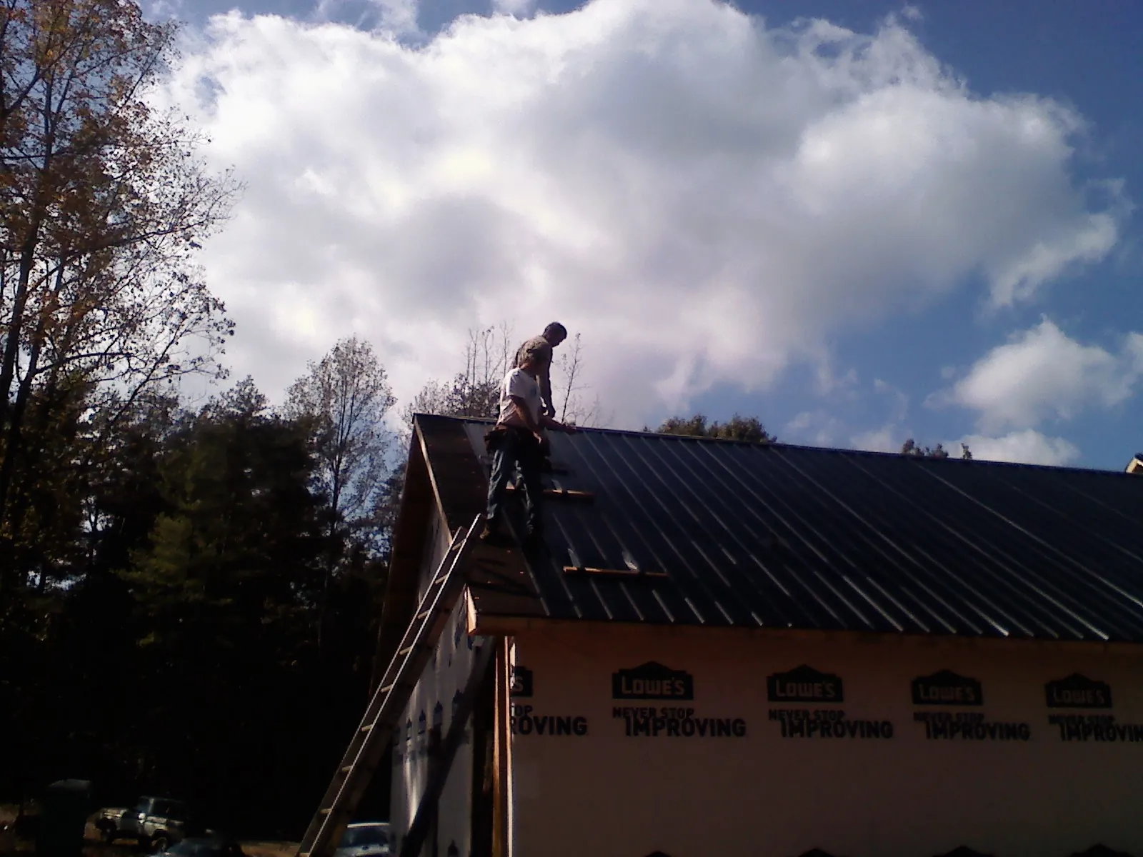 Roofer fastening dark metal panels high against a cloudy sky, from a Roof Inspection job in Baxley