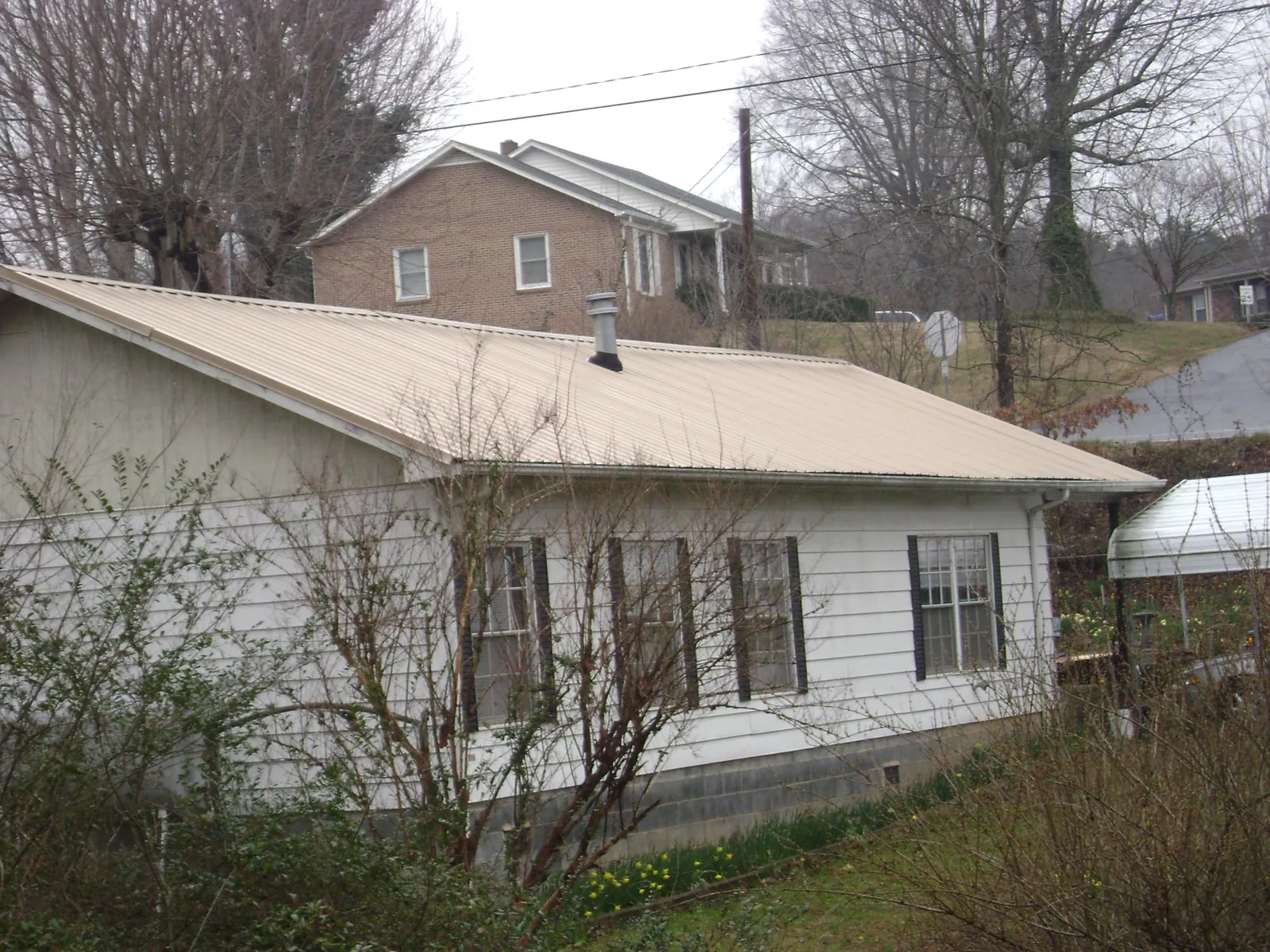 Tan metal roof on a white sided house set into a hillside — Commercial Roofing by Roofing Brothers in Baxley